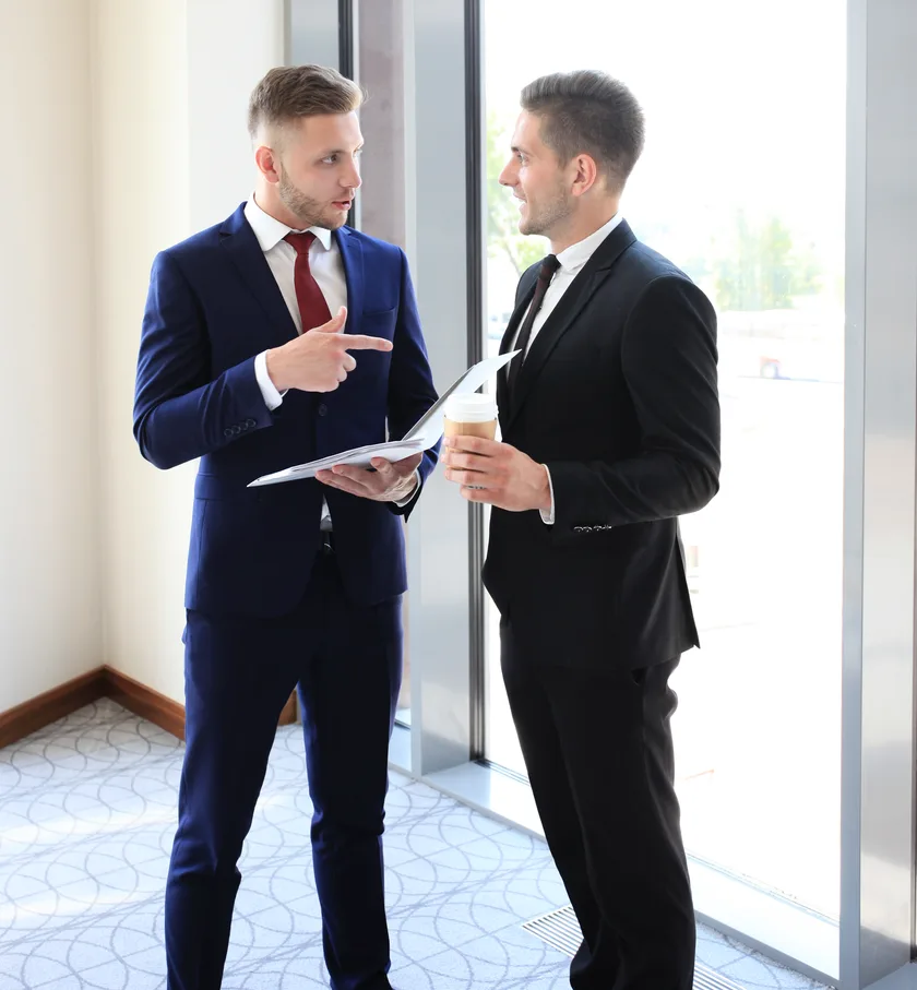 Two businessmen in suits discussing a document by a window